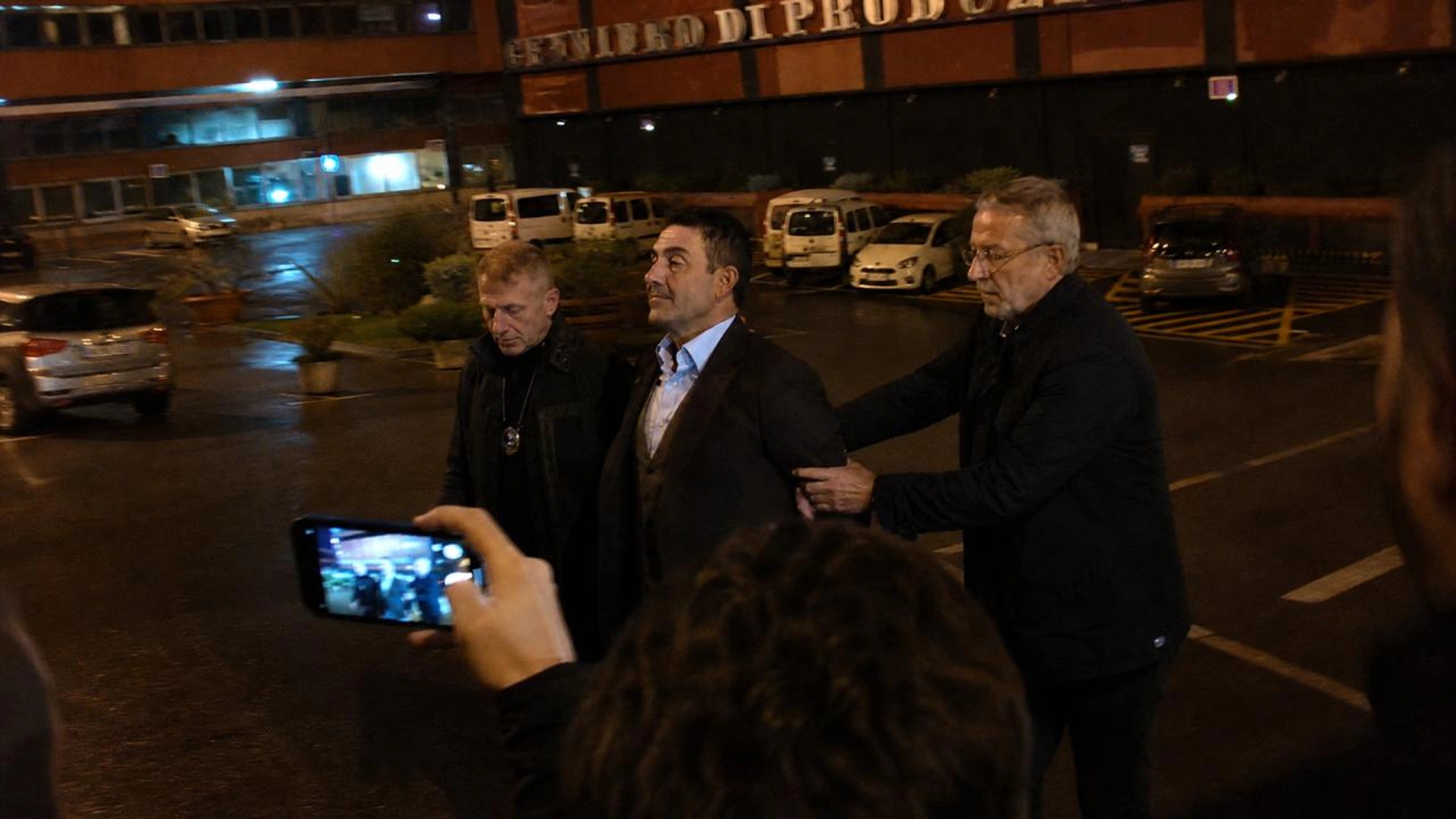 Roberto Vannacci circondato da persone con telefoni, agenti della Guardia di Finanza sullo sfondo.