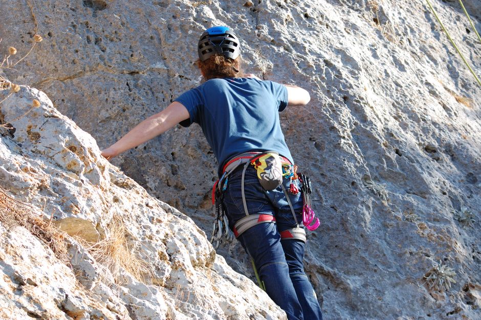 Rear view of a climber scaling a rocky wall outdoors, showcasing skill and courage.